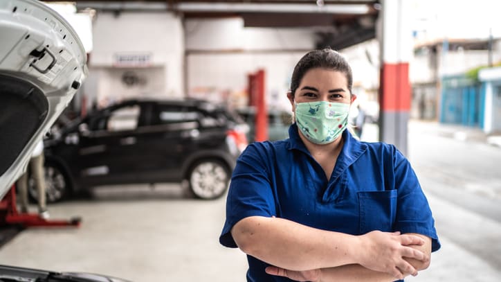 A woman wearing a face mask standing next to a car in a garage.