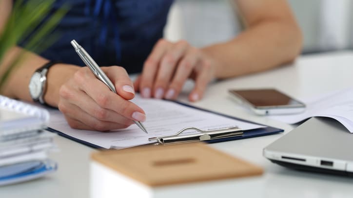 A woman is writing on a piece of paper with a pen.