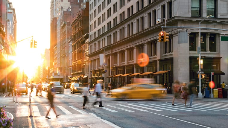 People crossing a street in new york city at sunset.
