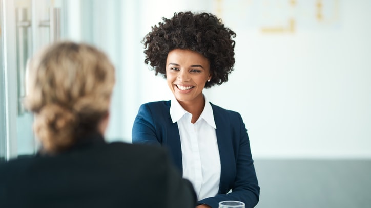 A woman in a business suit is shaking hands with another woman in an office.