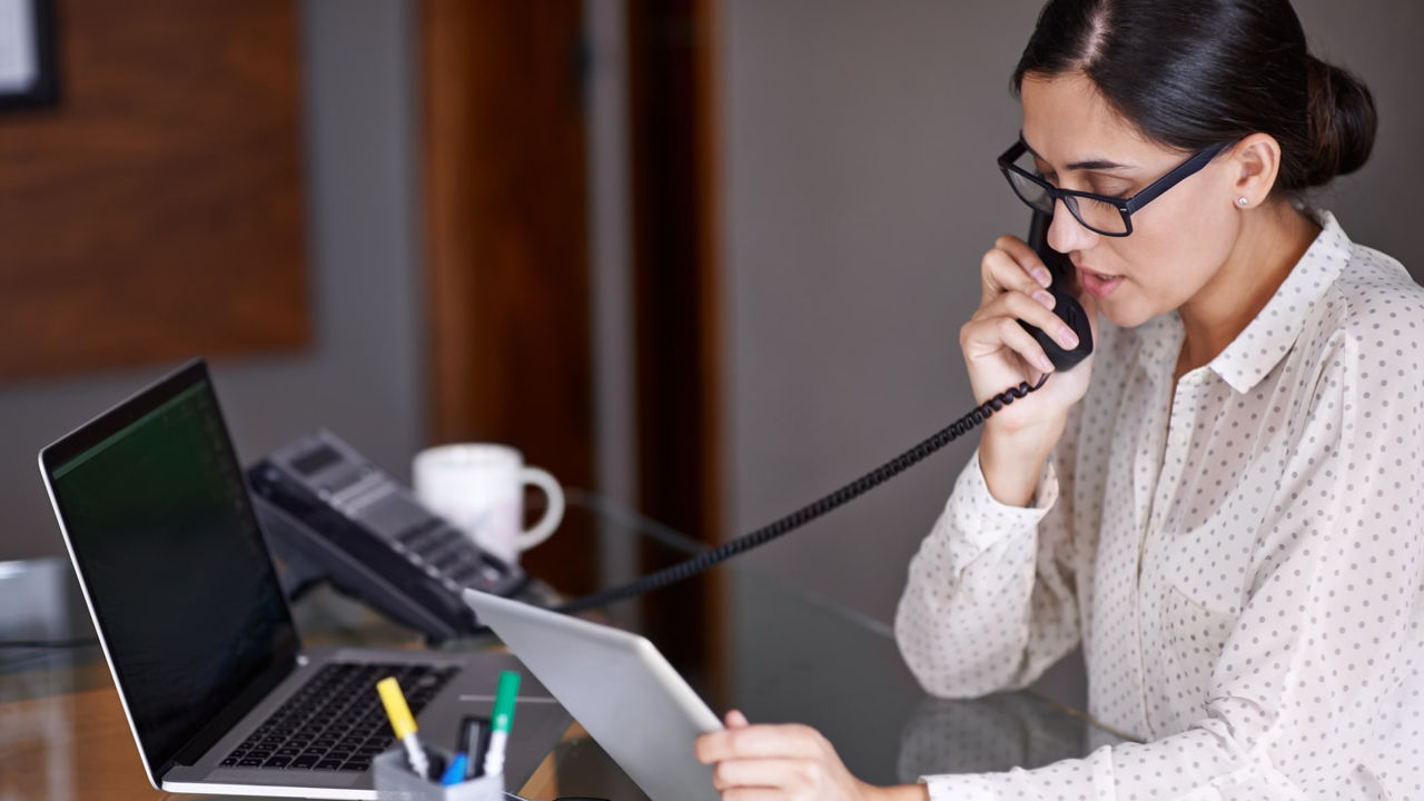 A woman is talking on the phone while sitting at her desk.