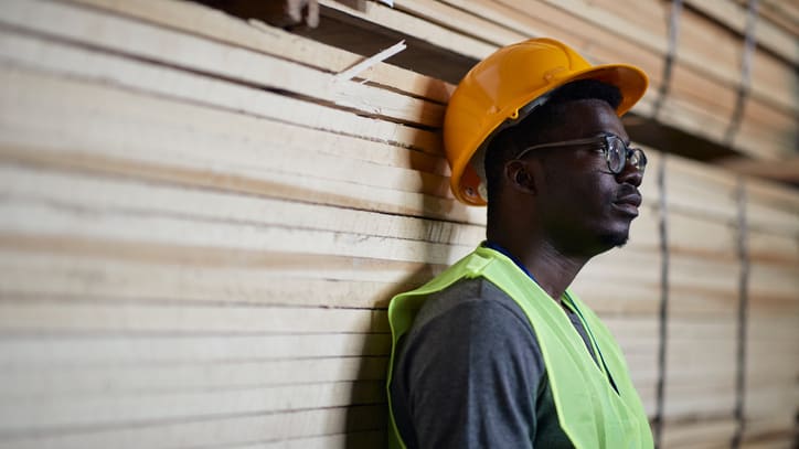 A man wearing a hard hat is leaning against a wooden wall.