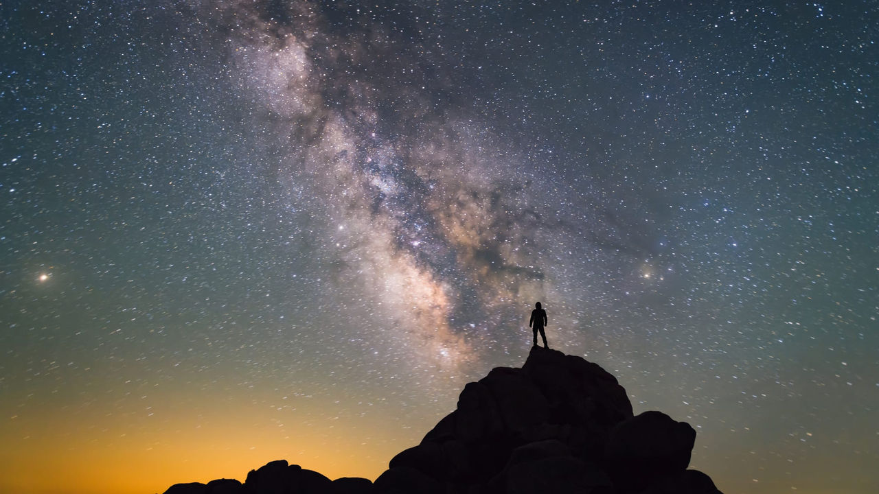 A man standing on top of a rock looking at the milky way.