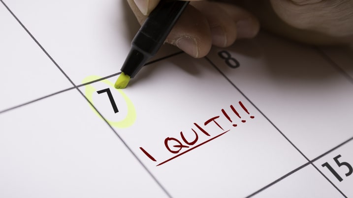 A person writing the word quit on a calendar.