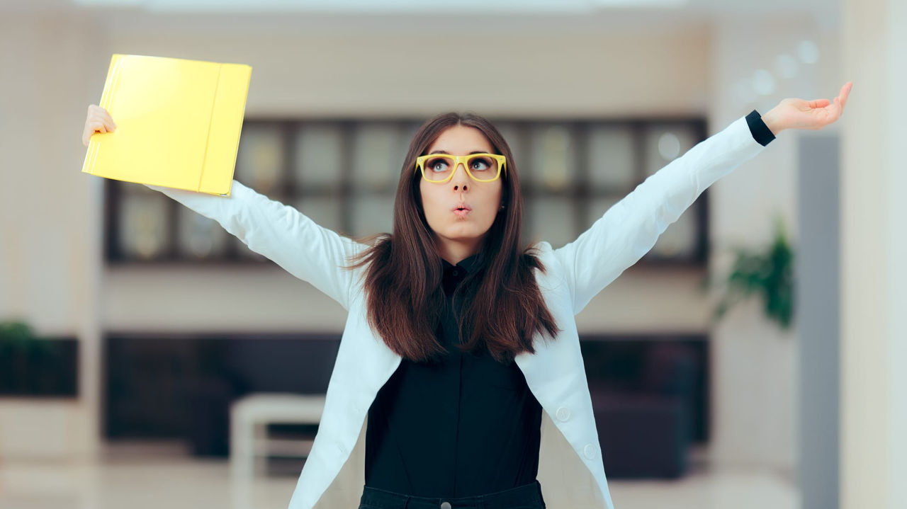 A woman in glasses is holding up a yellow folder.