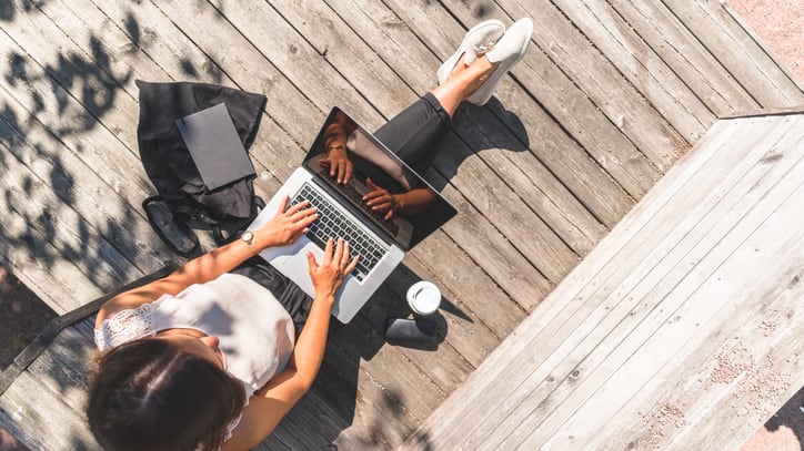 A woman using her laptop on a wooden deck.