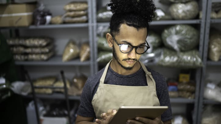 A man in an apron is using a tablet in a warehouse.