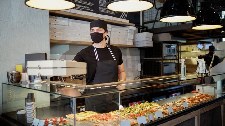 A pizza chef wearing a mask in front of a counter.