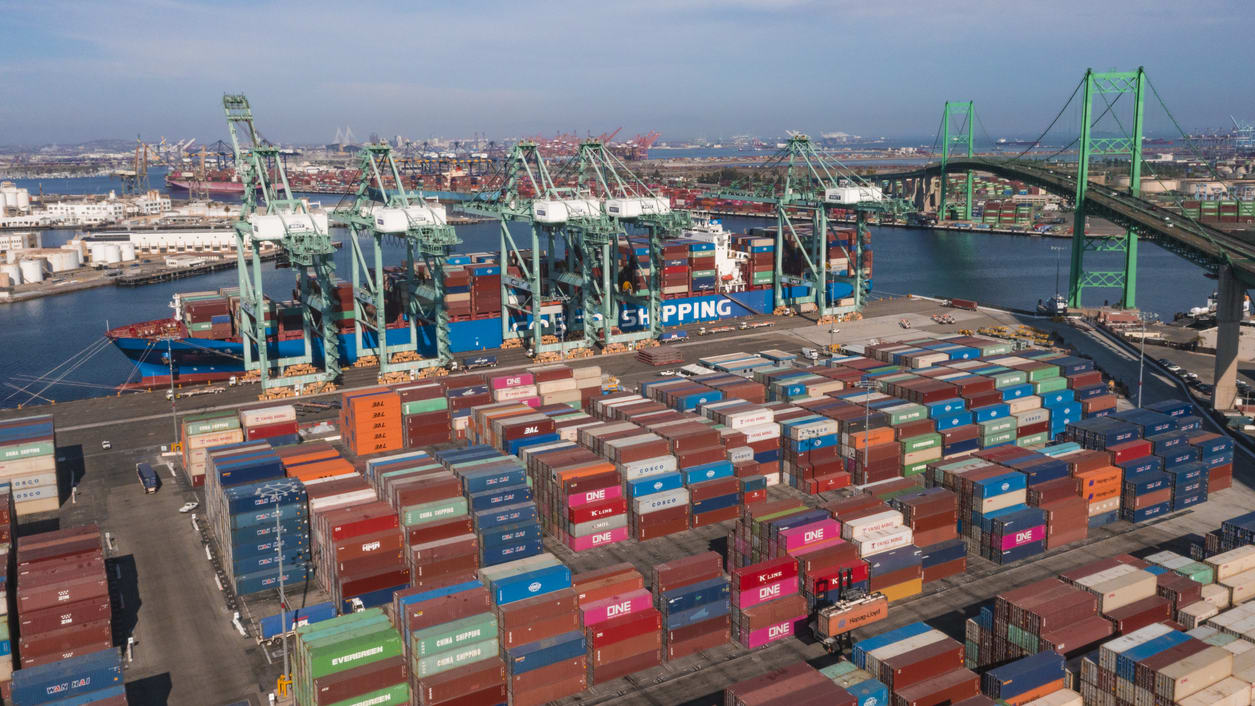 An aerial view of a container port with a bridge in the background.