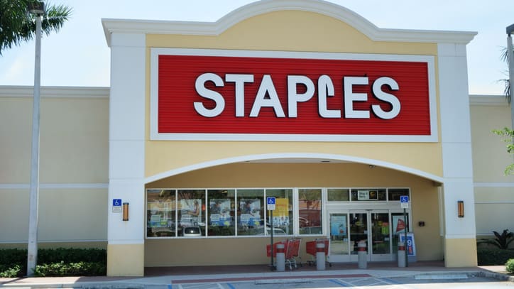 A staples store with cars parked in front of it.