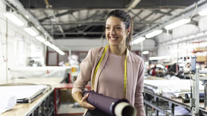A woman is standing in a factory holding a piece of fabric.
