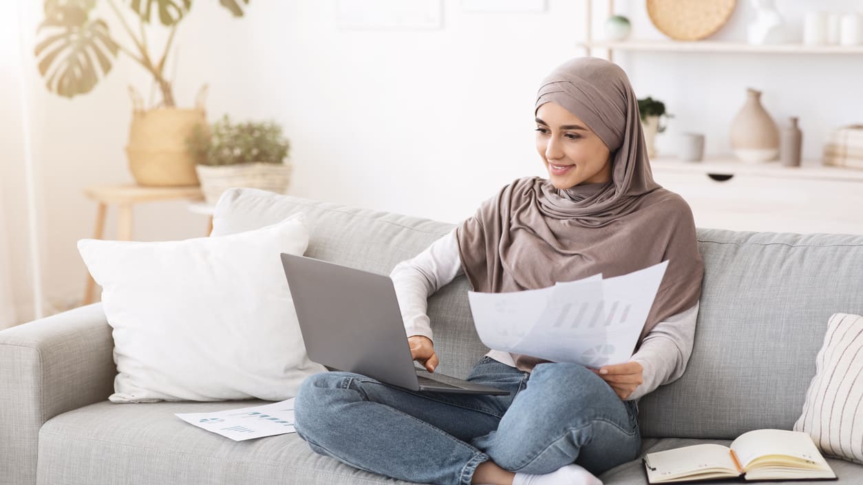 A young muslim woman sitting on a couch and working on her laptop.