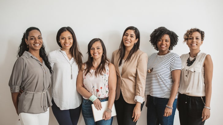 A group of women standing together in front of a white wall.
