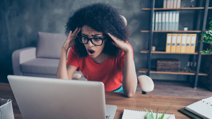 An afro-american woman is shocked while working on her laptop.