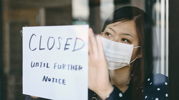 A woman wearing a face mask holding a sign that says closed.
