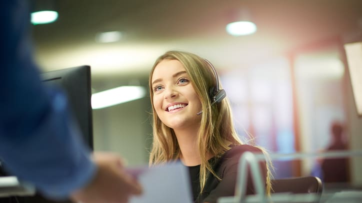 A woman in a headset is smiling at a computer.
