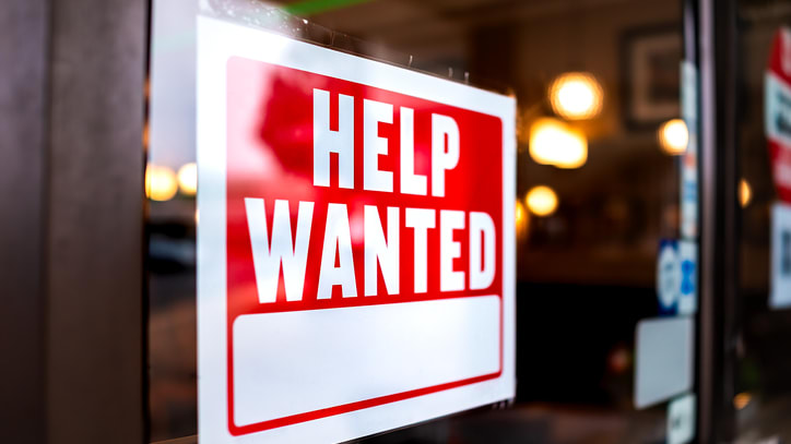 A sign that says help wanted on the door of a restaurant.