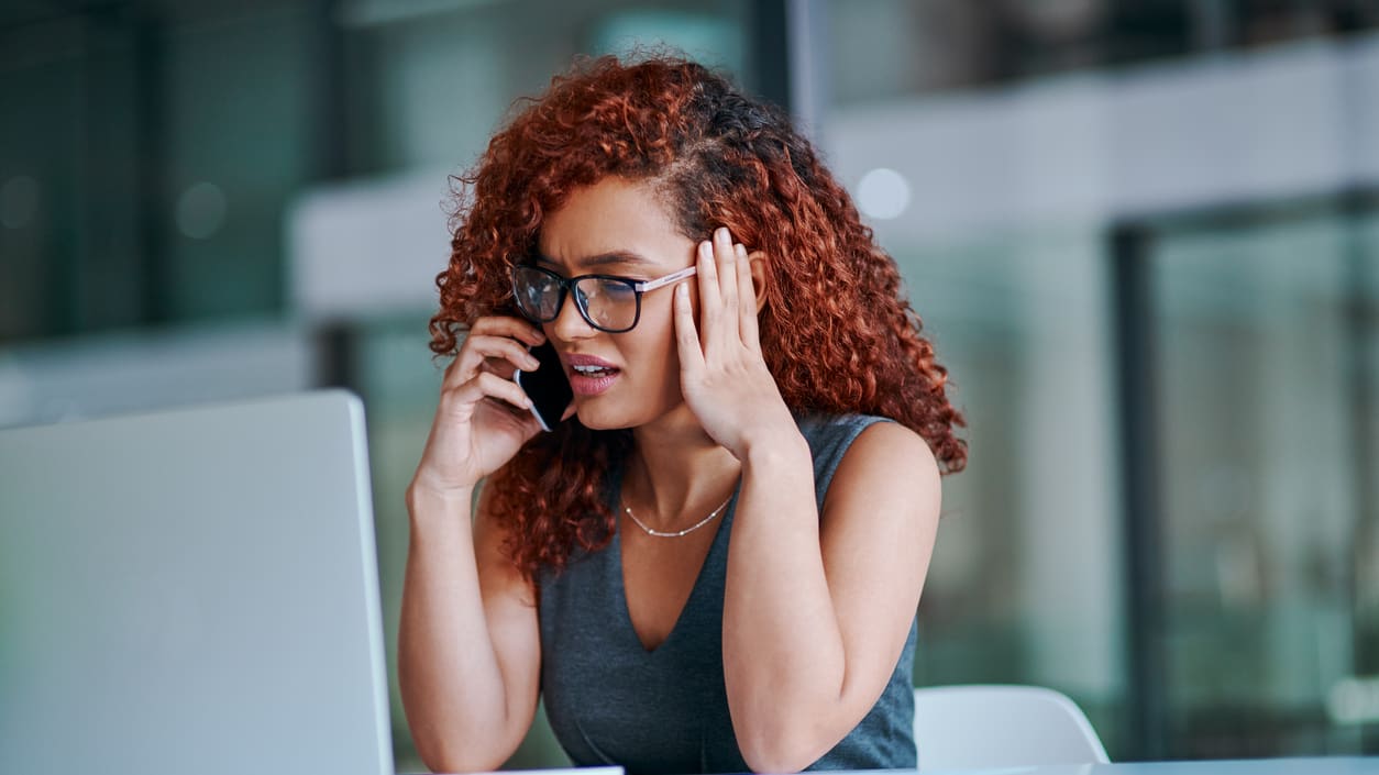 A woman is talking on the phone while sitting at a desk.