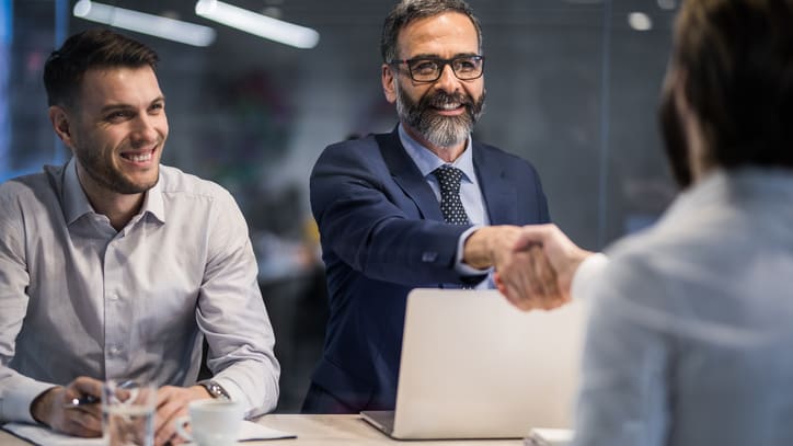 Two business people shaking hands while sitting at a table.