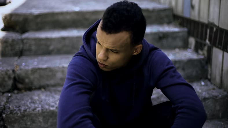 A young man in a blue hoodie sitting on steps.