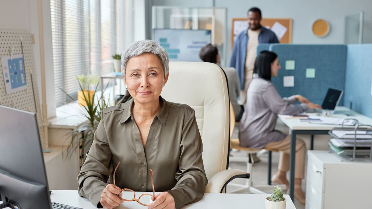 An older woman sitting at a desk in an office.