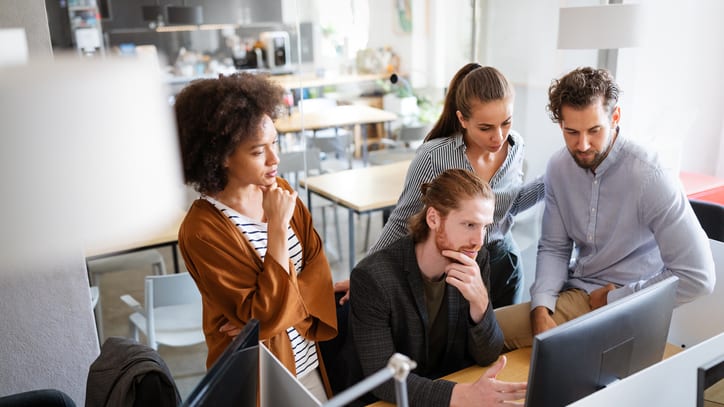 A group of people in an office looking at a computer.