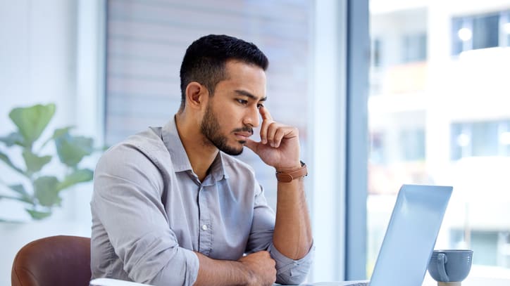 A man sitting at his desk looking at his laptop.