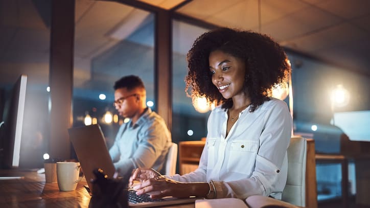 A woman and a man working on a laptop at night.