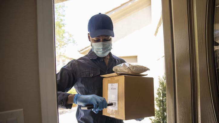A man wearing a mask and gloves is delivering a package to a house.