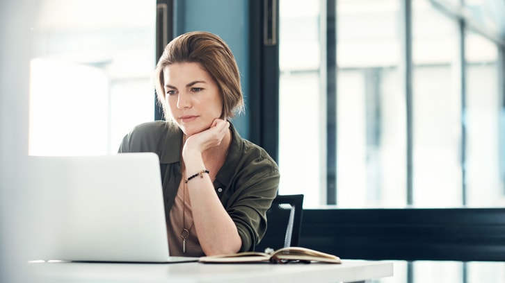 A woman sitting at a desk looking at her laptop.