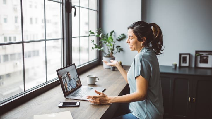 A woman sitting at a desk with a laptop in front of a window.