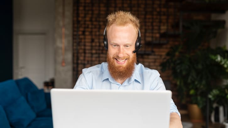 A man with a beard is using a laptop at home.