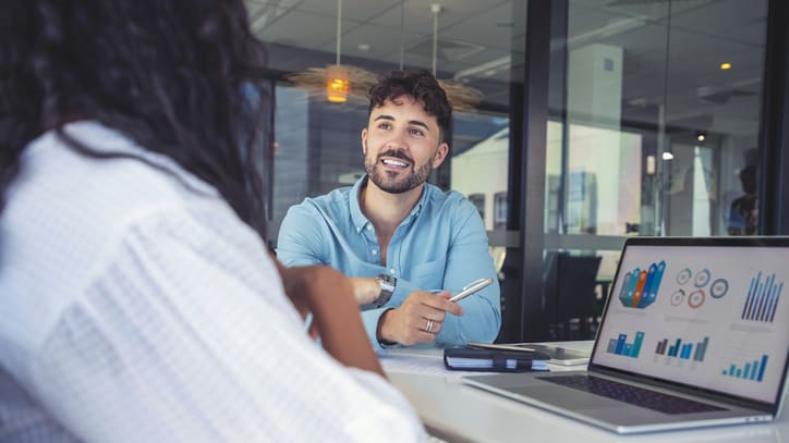 Two business people sitting at a table with graphs on their laptops.