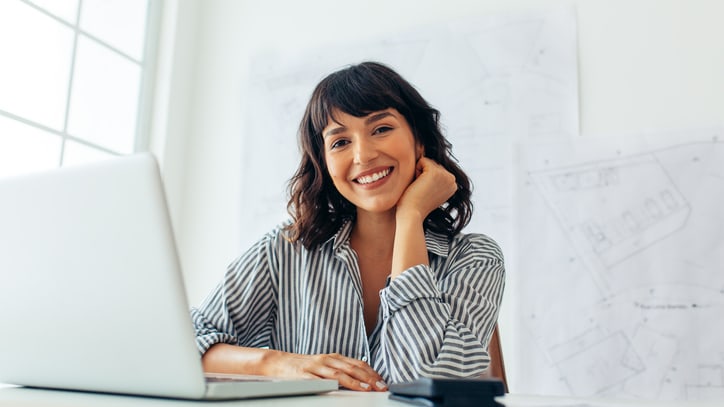 A smiling woman sitting at a desk with a laptop in front of her.