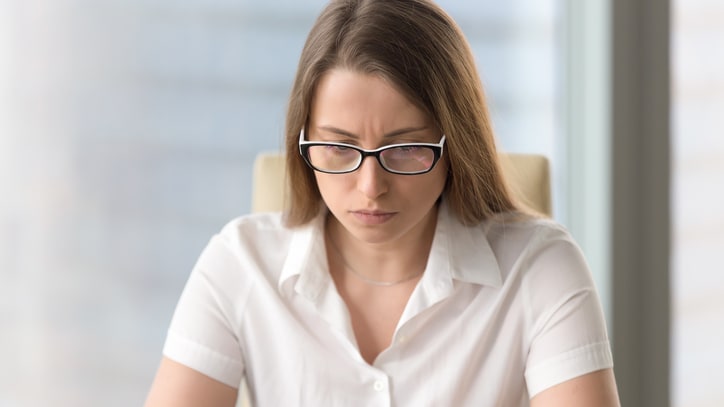 A woman in glasses sitting at a desk using a laptop.