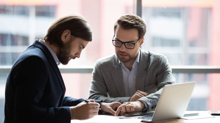 Two businessmen sitting at a table and talking to each other.