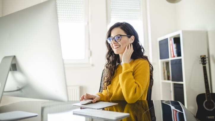 A woman wearing glasses is sitting at a desk in front of a computer.