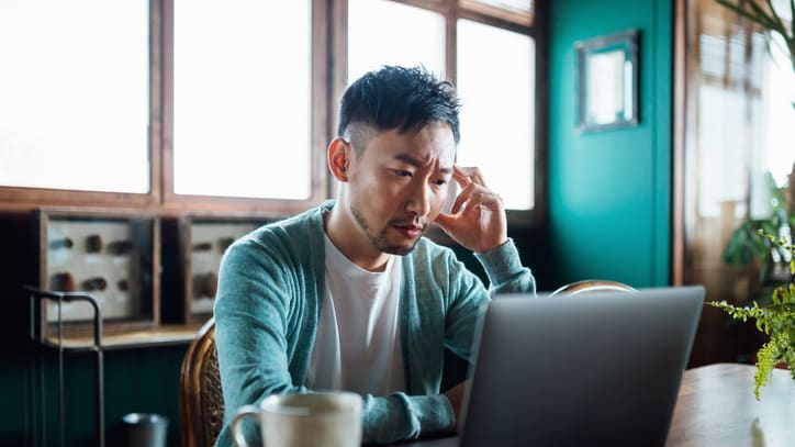 A man sitting at a table looking at his laptop.