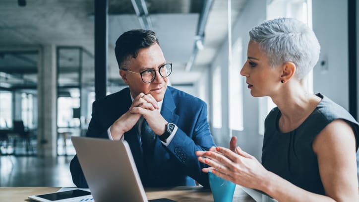 Two business people talking on a laptop in an office.