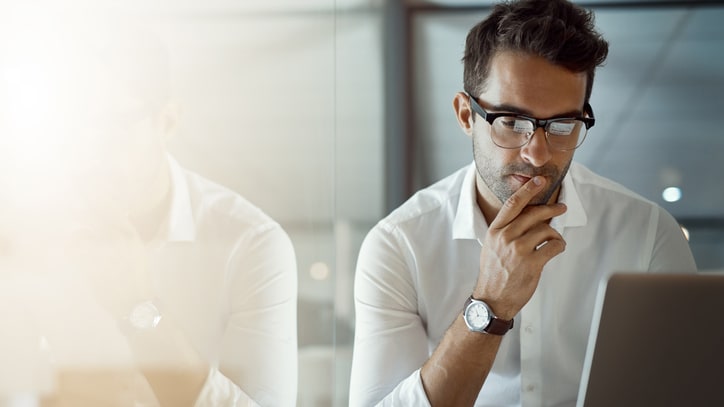 A man in glasses is sitting in front of a laptop.