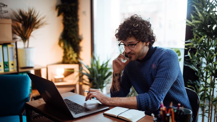 A man talking on the phone while sitting at a desk with a laptop.