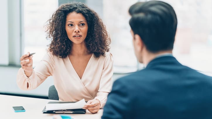 A woman is talking to a man at a meeting.