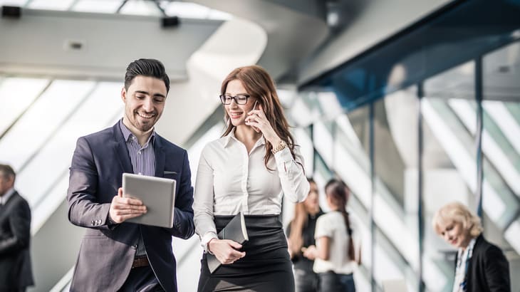 Two business people walking in an office with a tablet computer.