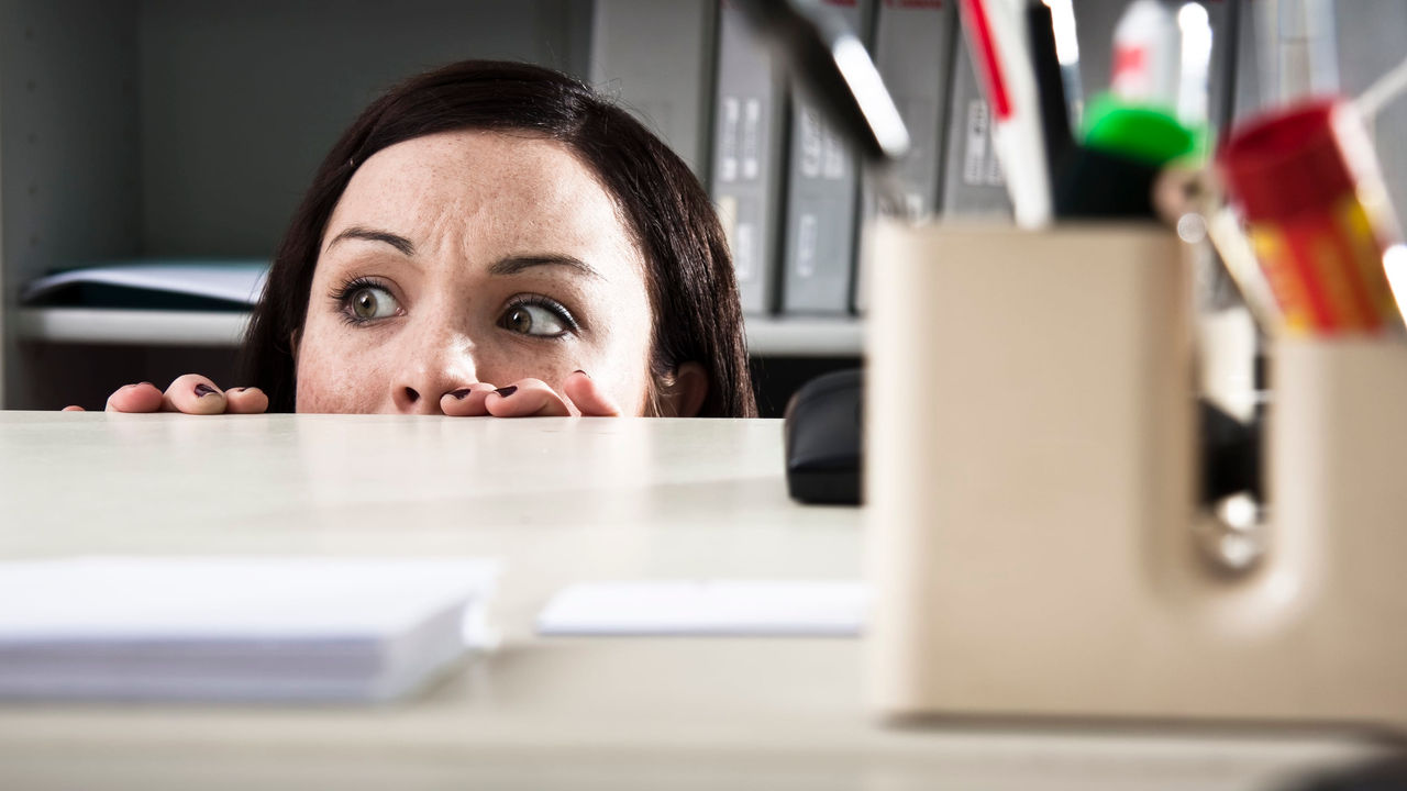 A woman peeking over a desk in an office.