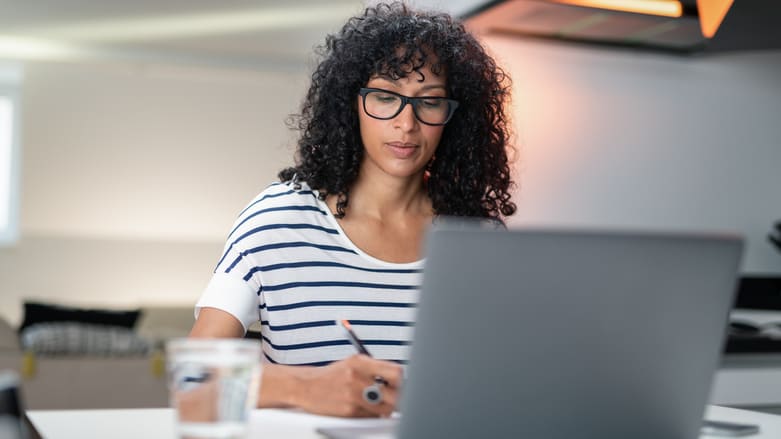 A woman wearing glasses is sitting at a desk with a laptop.