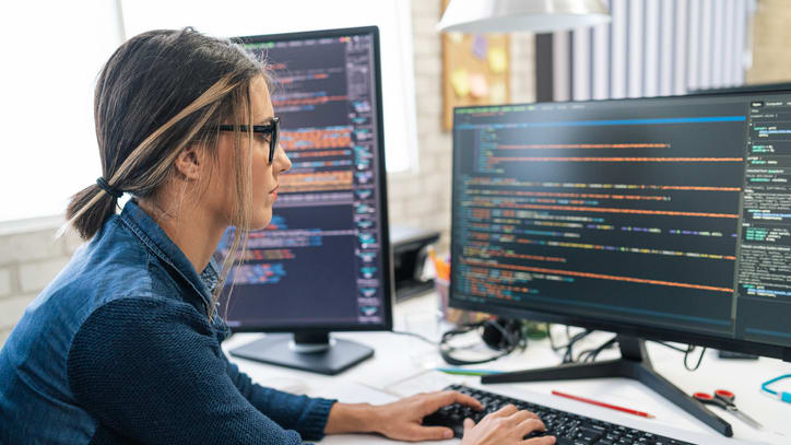 A woman is working on a computer with two monitors.