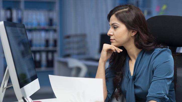 A woman sitting at a desk and looking at a piece of paper.