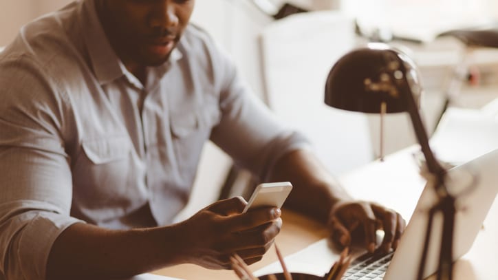 A man sitting at a desk with a laptop and cell phone.