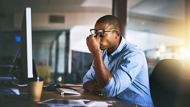 A man in glasses is sitting at a desk with a computer in front of him.