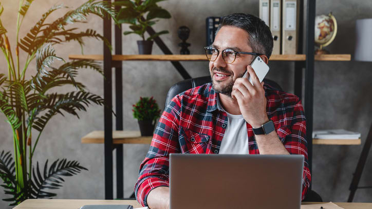 A man is talking on the phone while sitting at his desk.